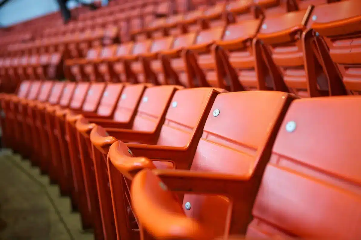 Mano anonima con racchetta e smartphone su panchina vicino a borsa sportiva, stadio sfocato