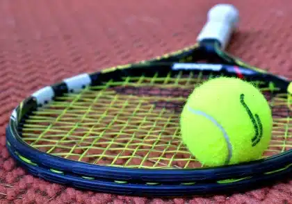 Palla da tennis vicino alla linea di fondo con una racchetta in primo piano su un campo anonimo