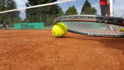 Due racchette e una palla su cemento con luci di uno stadio sullo sfondo