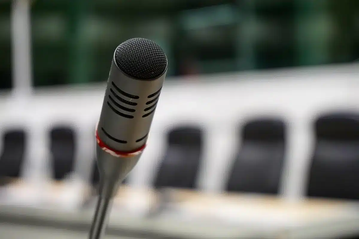 Conferenza stampa F1 con microfoni su un tavolo e giornalisti sullo sfondo